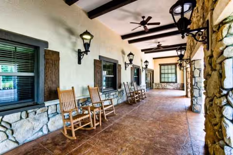 Covered outdoor corridor with wooden rocking chairs, stone walls, and ceiling fans.