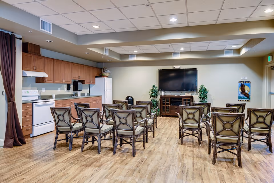 Community common room with rows of chairs facing a wall-mounted TV and a kitchenette along the left wall.