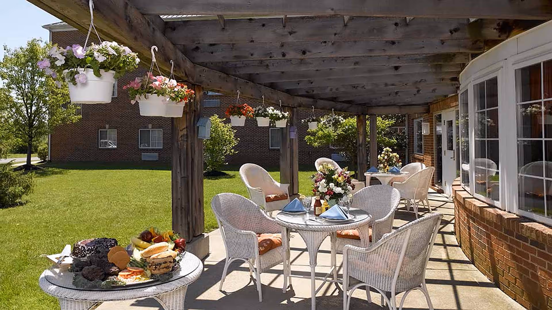 Covered outdoor patio with wicker tables and chairs set for dining and hanging flower baskets.