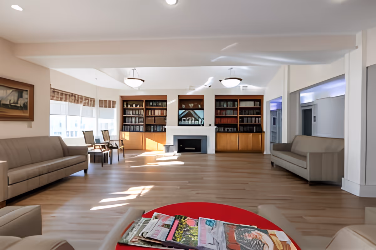 Spacious communal living room with sofas, bookshelves, a fireplace and a table with magazines in the foreground.