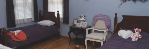 A bedroom with two single beds, a chair, and a nightstand in a shared senior room.