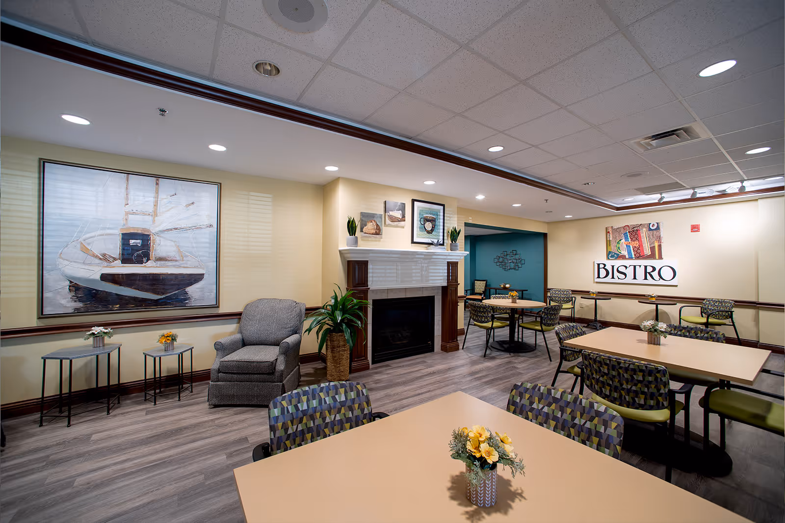 Bright bistro-style dining area with tables and patterned chairs, a fireplace, artwork, and a 'BISTRO' sign on the wall.