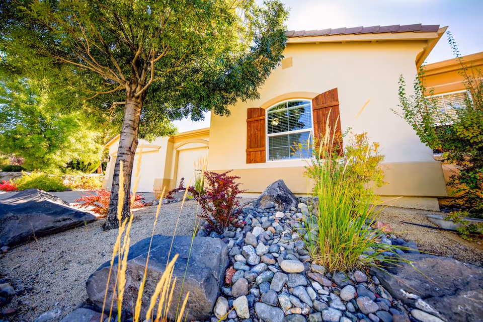 Front exterior of a beige stucco senior living facility with arched window and rock landscaping.