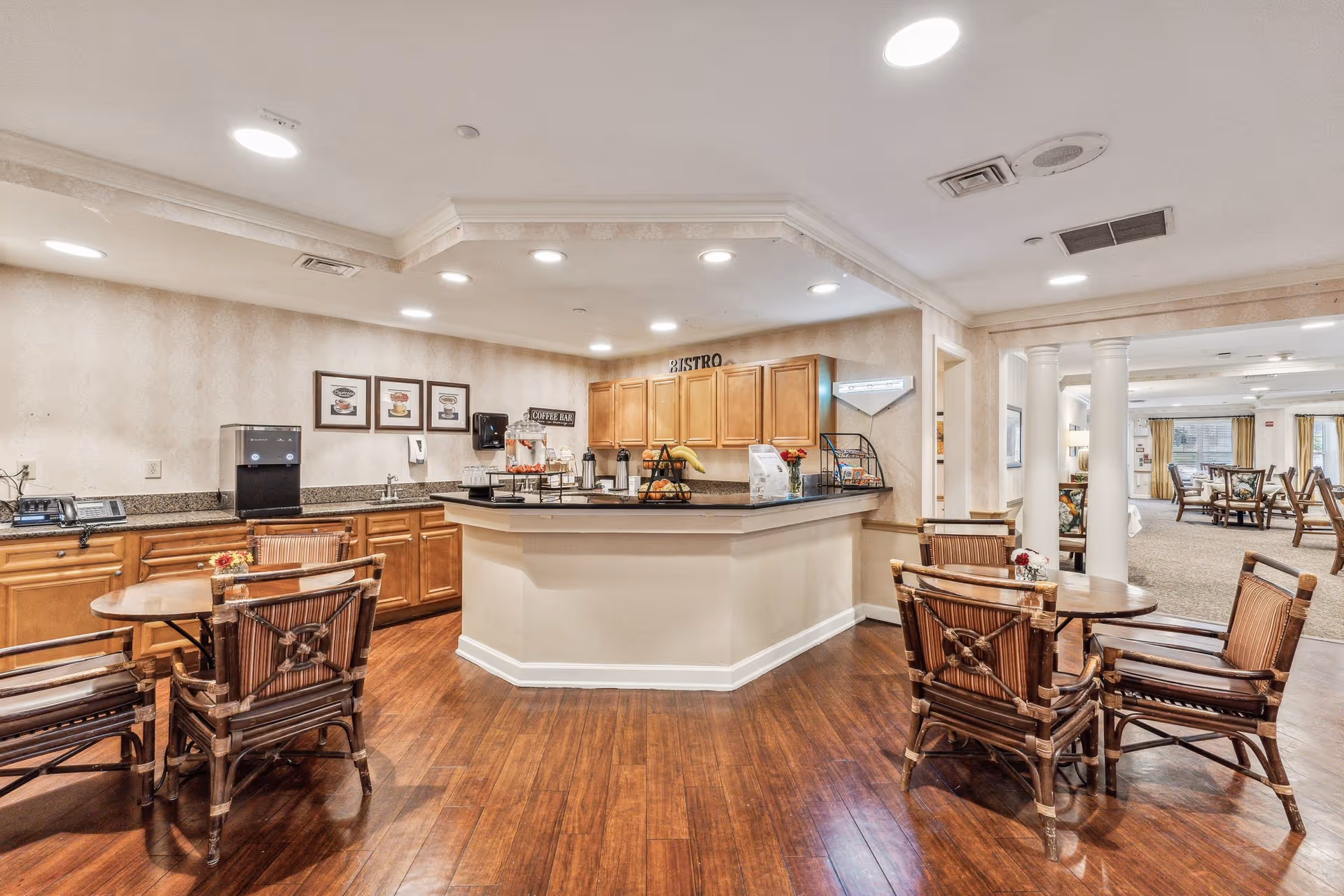 Communal bistro area with a service counter, wooden tables and chairs, and warm overhead lighting.