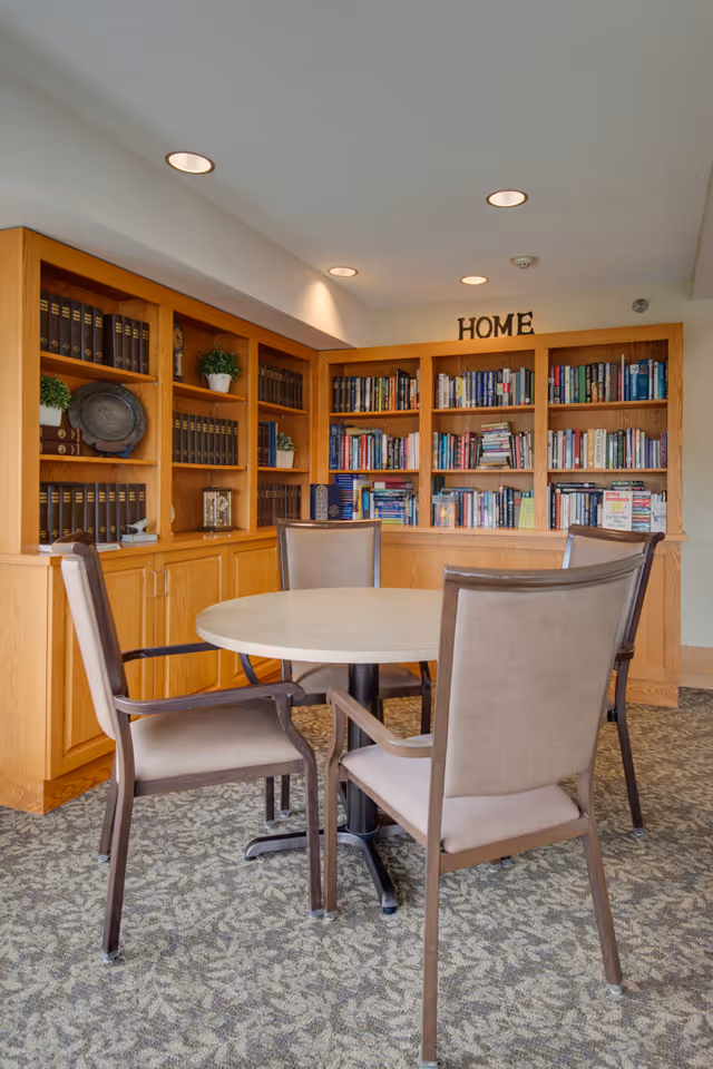 Small communal reading area with a round table, four chairs, and built-in bookshelves labeled 'HOME'.