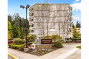 Exterior view of a multi-story residential building surrounded by trees and landscaped greenery. A sign in front reads 'CRISTWOOD PARK'. The sky is clear and blue.