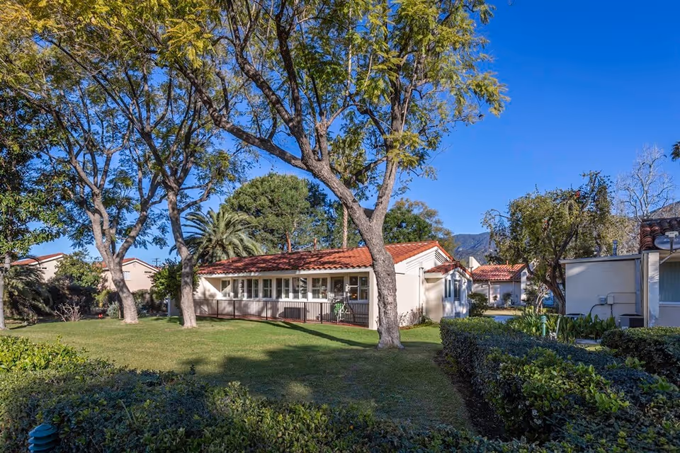Single-story building with a red tile roof surrounded by green grass, trees, and shrubs under a clear blue sky at Westminster Gardens.