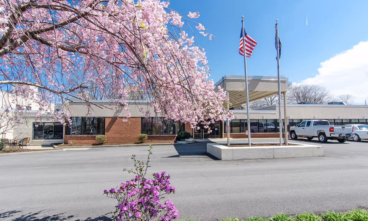 Exterior view of the Twinbrook Healthcare and Rehabilitation Center with blooming trees and flags.