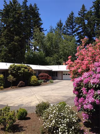 Exterior view of a senior living facility surrounded by lush greenery and flowering shrubs.