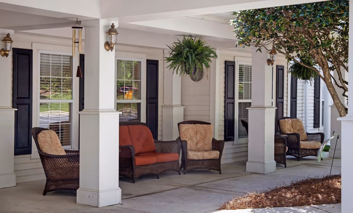 Covered porch with white columns featuring wicker chairs and a red-cushioned loveseat beneath hanging ferns.