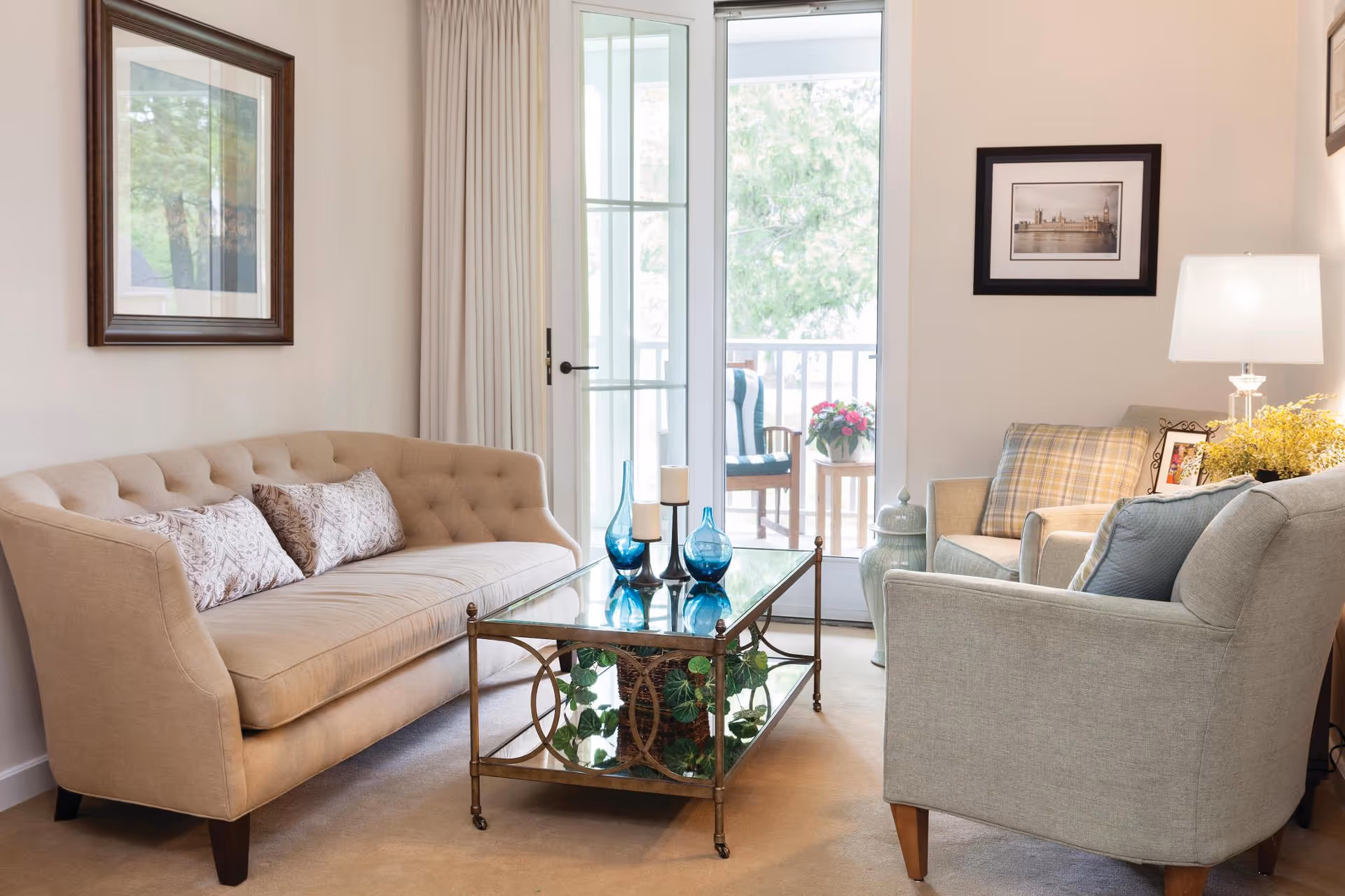 Bright furnished living room with a tufted sofa, armchairs, glass coffee table, and a door opening to a balcony.