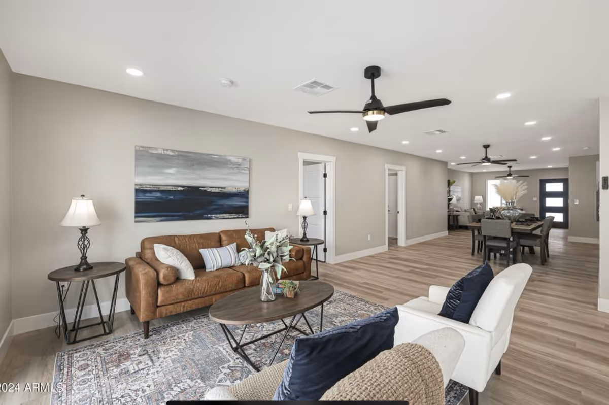 Open-concept living and dining area with a leather sofa, armchairs, coffee table and dining table in a modern neutral interior.