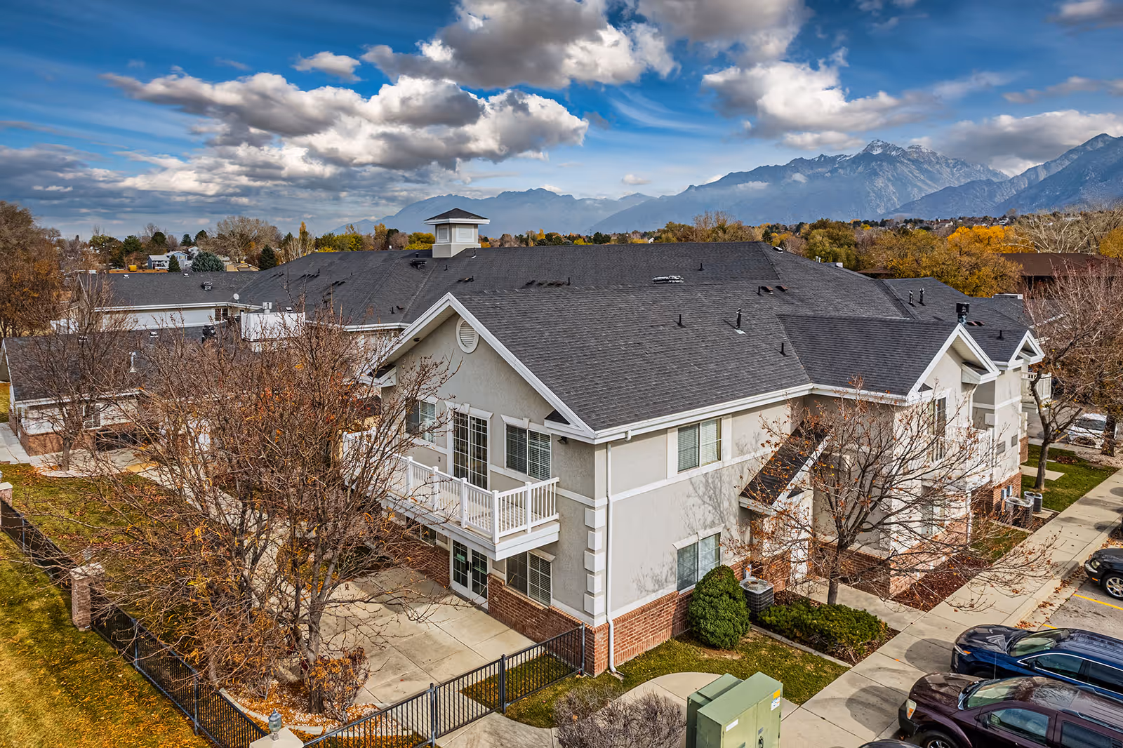 Aerial view of a two-story senior living building with white balconies, parking spaces, and mountains in the background.