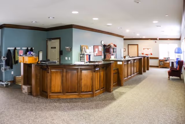 Spacious reception area with a long wooden front desk, carpeted floor, shelving and seating along the walls.