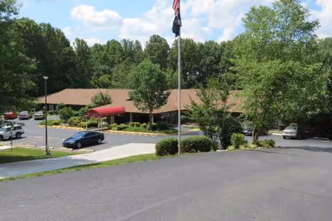 Exterior view of Four Oaks Healthcare Center with parked cars, flagpole, and surrounding trees.