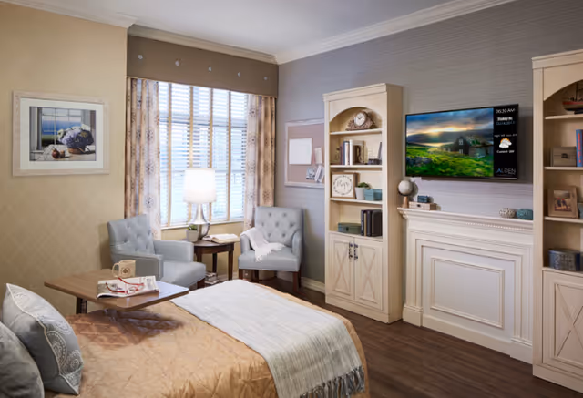 Cozy senior living bedroom with a seating area, bed, TV, and built-in cabinets.