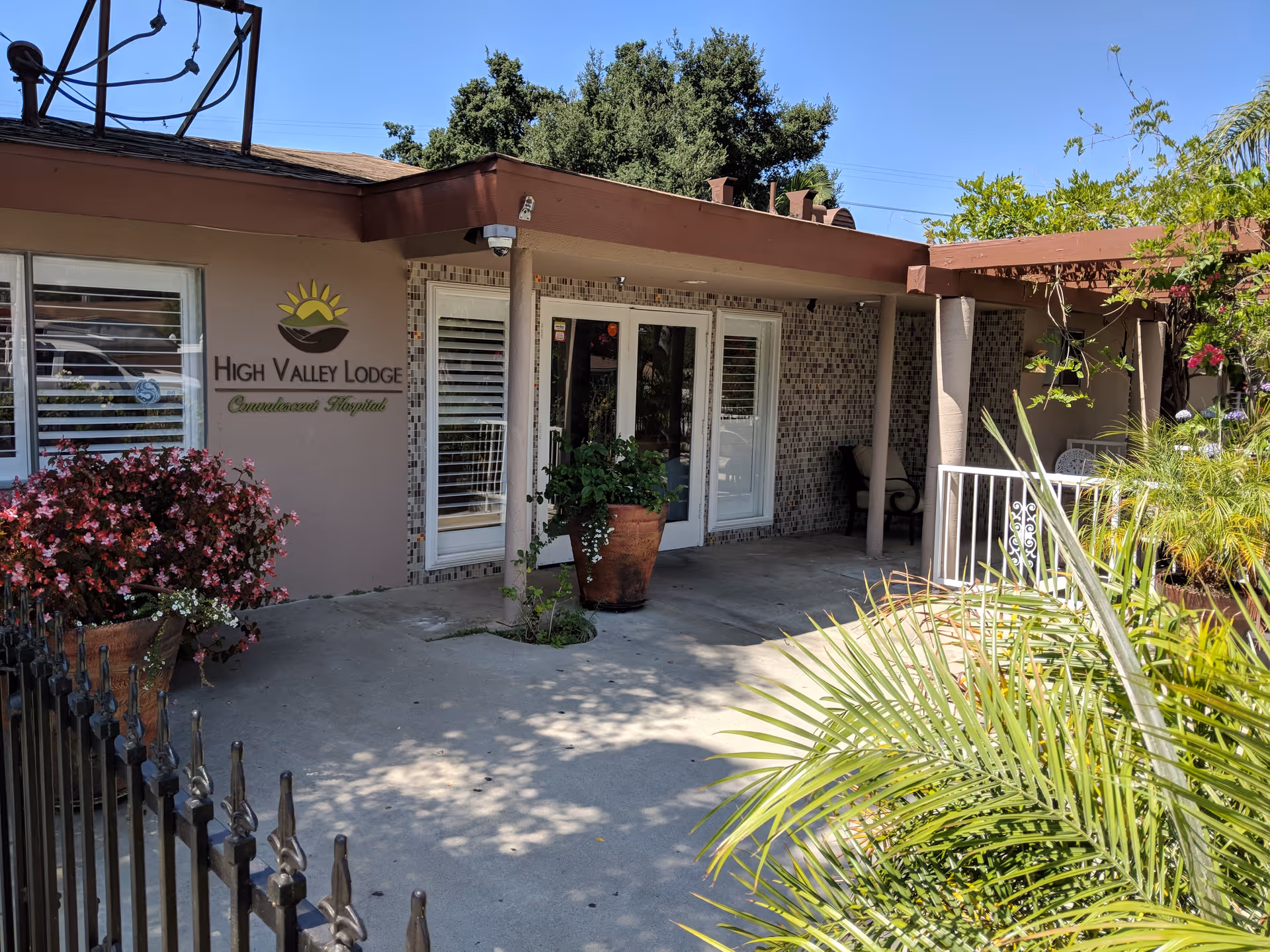 Front entrance of High Valley Lodge convalescent hospital with potted plants, a tiled entryway, and the facility sign on the wall.