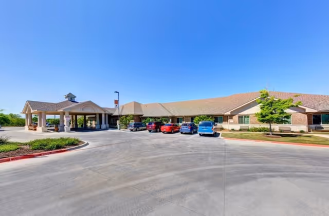 Exterior view of Hunters Pond Rehabilitation and Healthcare Center showing a single-story building with a covered entrance, several parked cars, and a clear blue sky.
