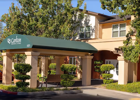 Entrance of Carlton Senior Living Sacramento Atrium Building with green awning and benches.