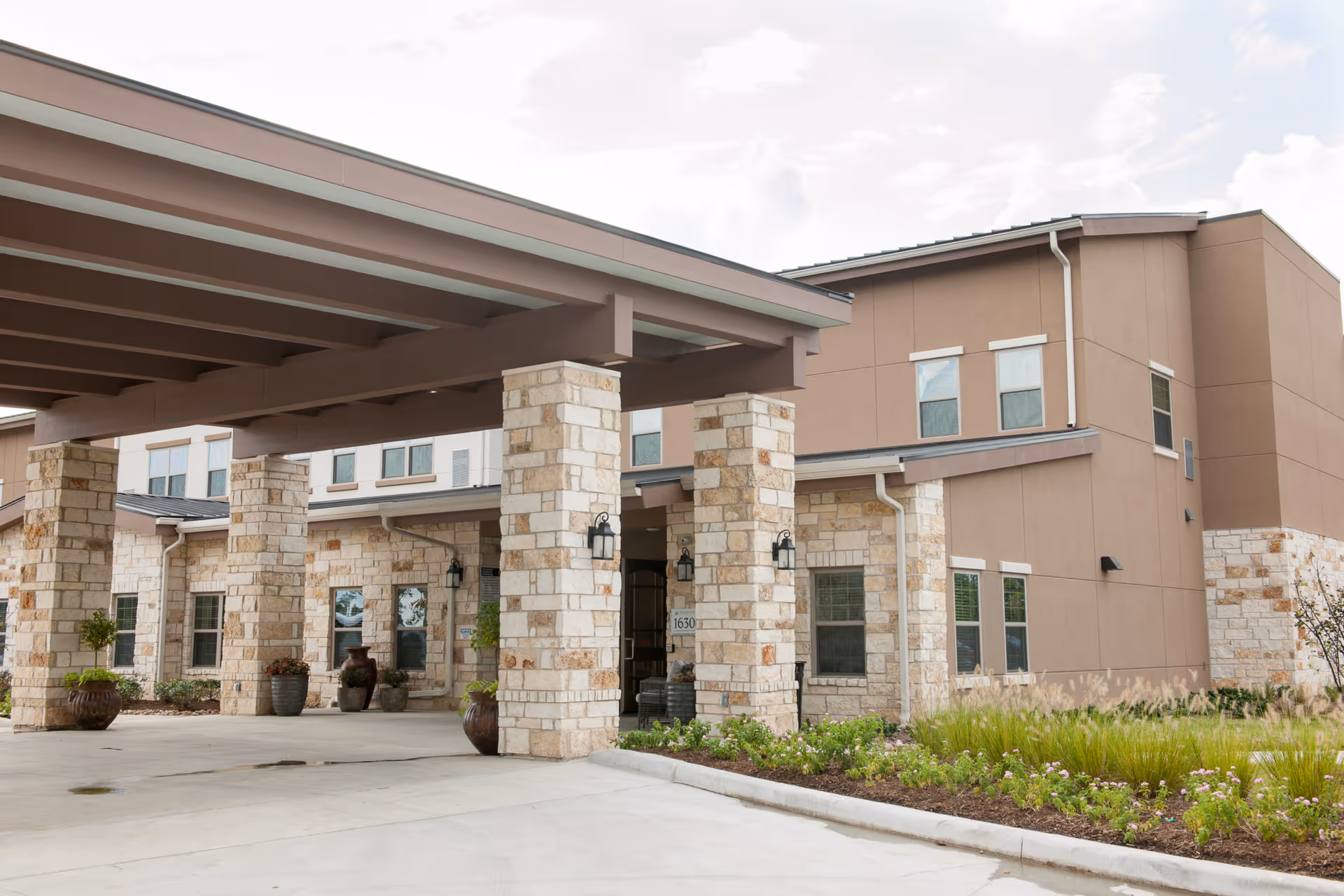 Entrance of the Spring Cypress Senior Living building with a covered porte-cochere supported by stone columns.
