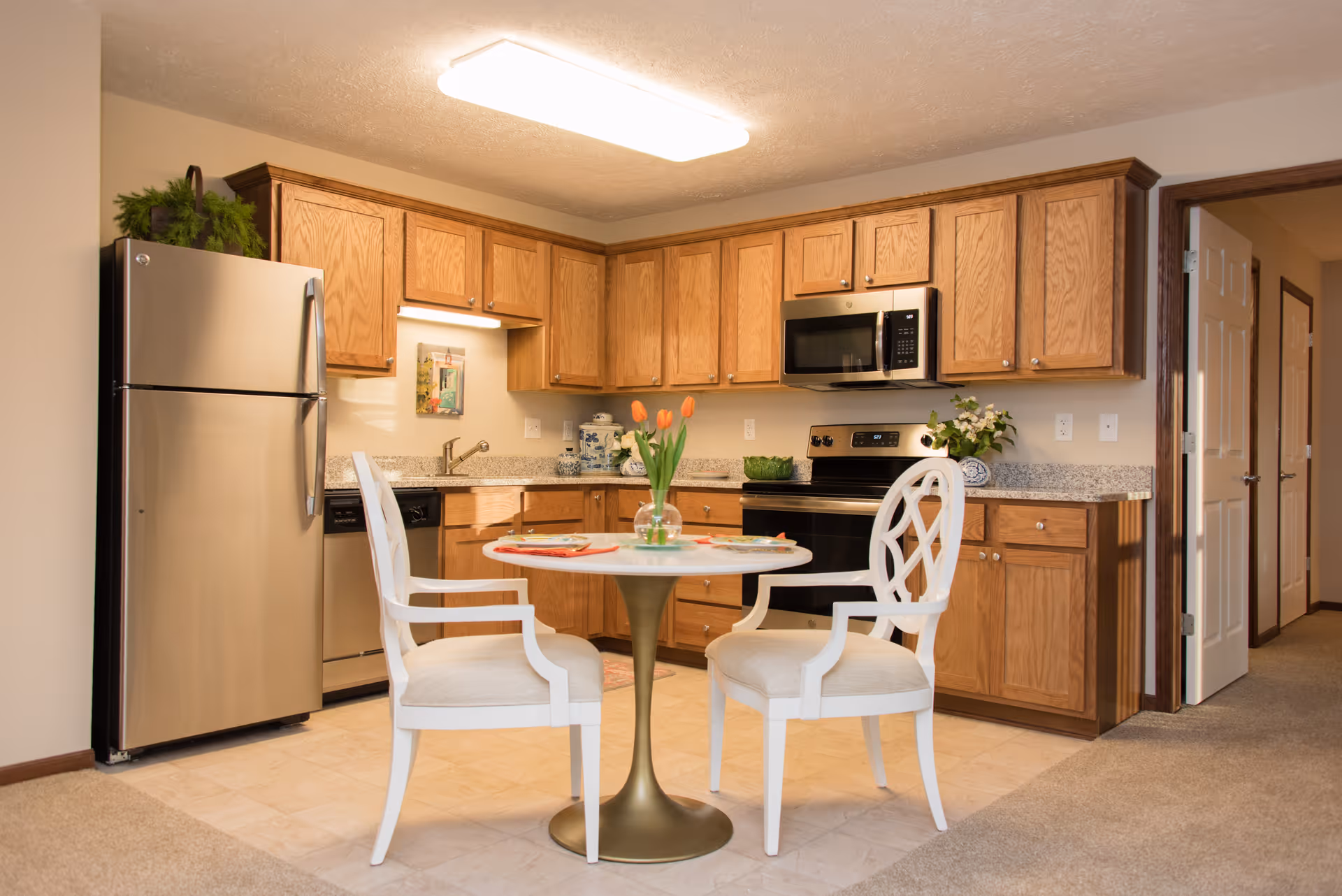 Small kitchen with wooden cabinets, stainless steel appliances and a round table with two white chairs.