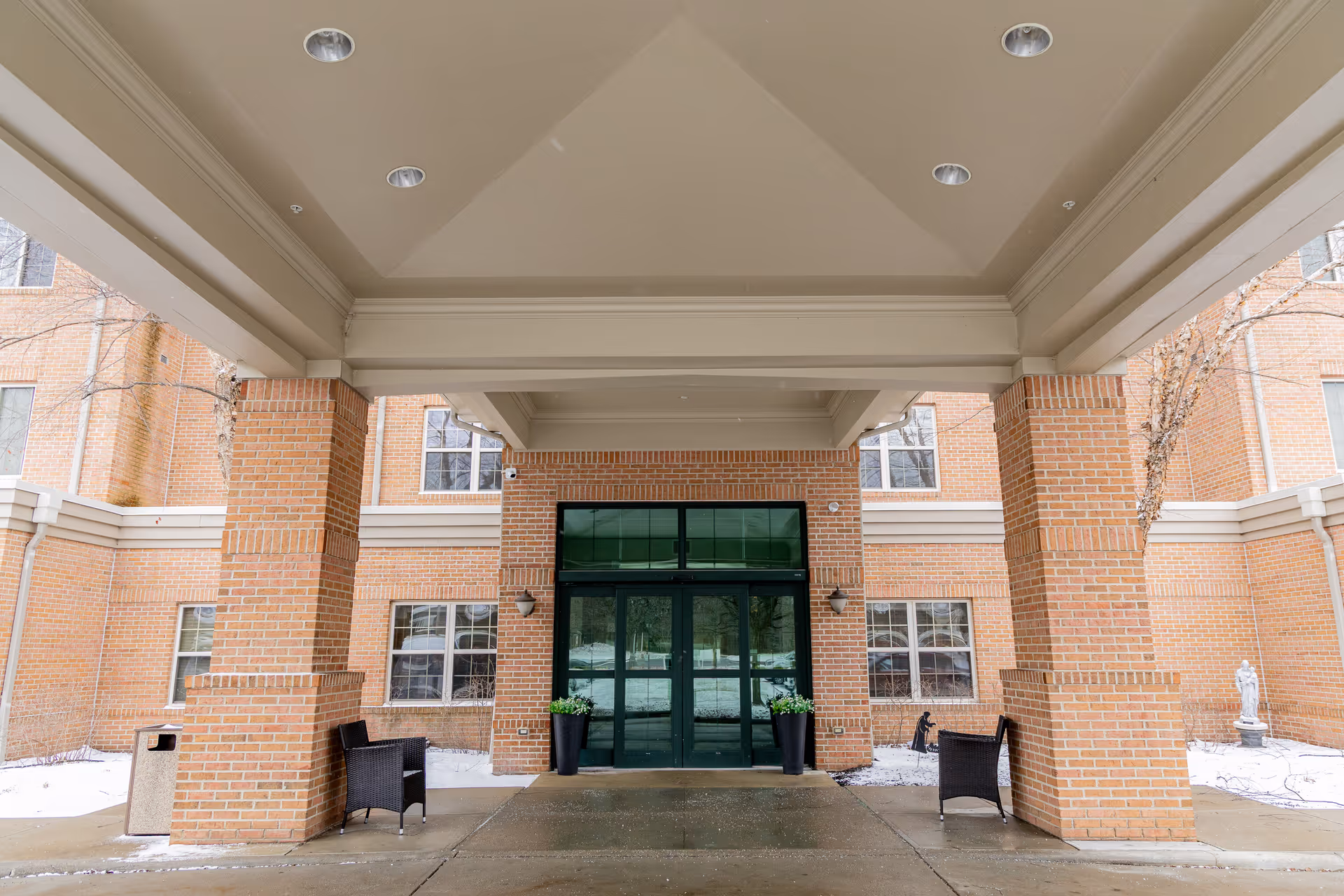 Covered brick porte-cochere with columns, seating, and glass double doors at the building entrance.