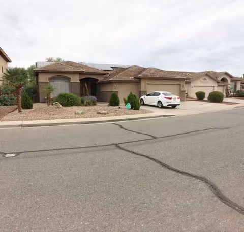 Single-story beige assisted living facility front with desert landscaping, a white car, and street view.