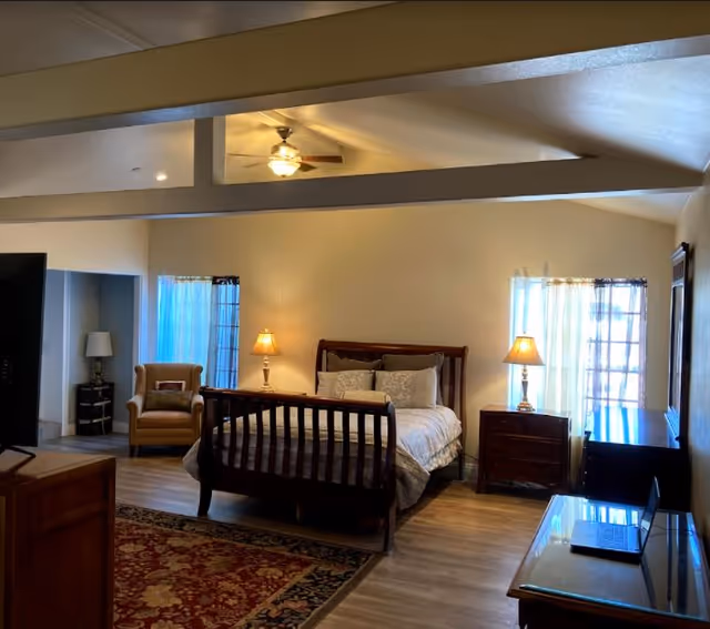 A spacious bedroom with a wooden bed, two nightstands, lamps, and an armchair.