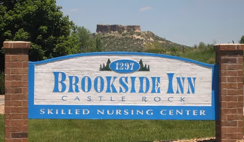 Outdoor sign for Brookside Inn Skilled Nursing Center in Castle Rock, with a natural landscape and a rocky hill in the background.