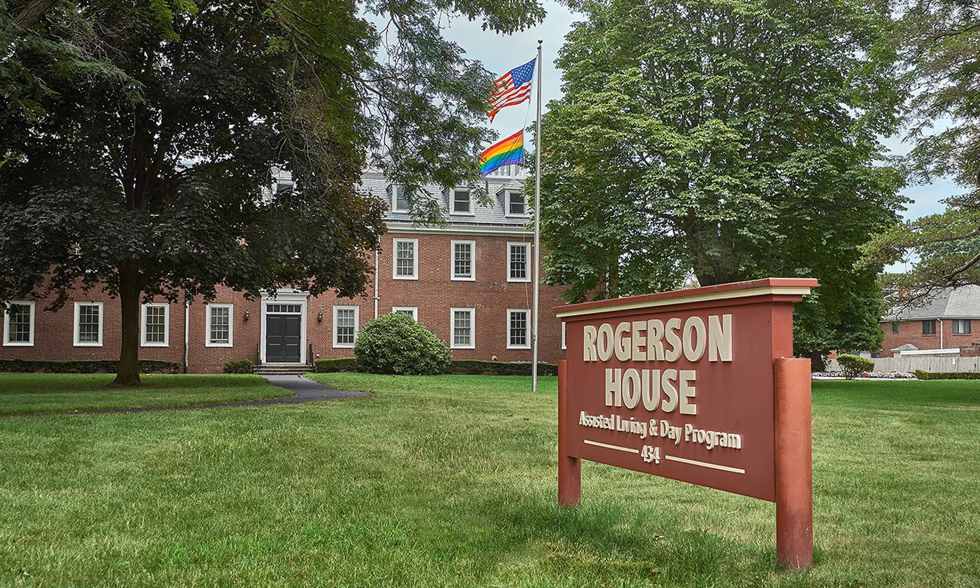 Brick building with manicured lawn, two flagpoles, and Rogerson House sign in foreground.