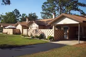 Exterior view of Cecil Pines: single-story brick cottages with a covered entrance and green lawn.