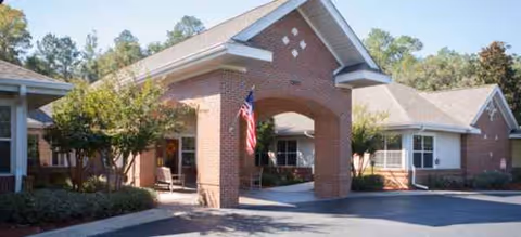 Brookdale-style senior living facility entrance with archway, flag, and trees.