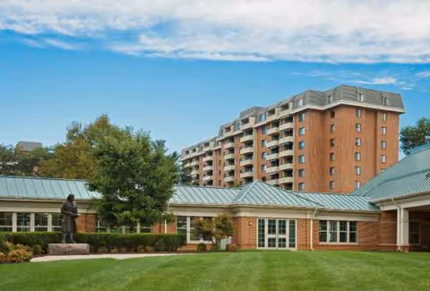 Exterior view of Kindley Assisted Living facility with brick buildings, green lawn, and statue.