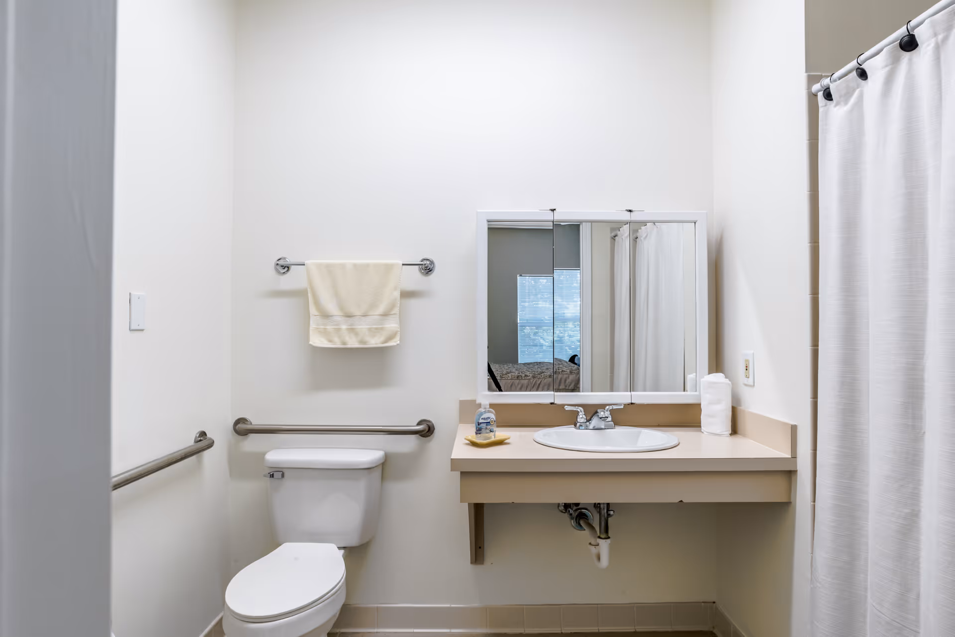 Accessible bathroom with a toilet, grab bars, sink and mirror, and a shower with a curtain.