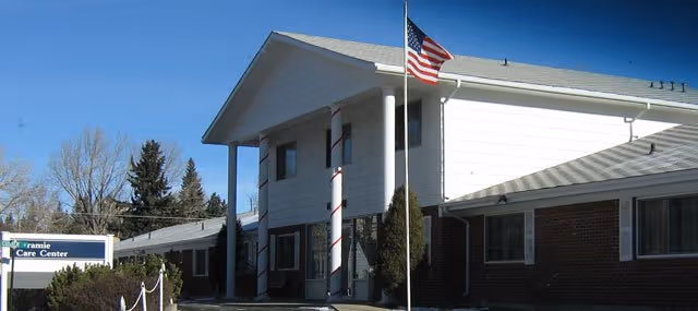 Front view of Laramie Care Center with flag, white siding and brick base.