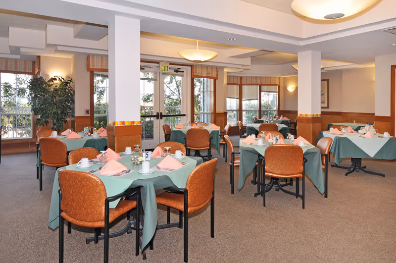 Dining room with multiple tables set with green tablecloths, pink napkins, and orange chairs.