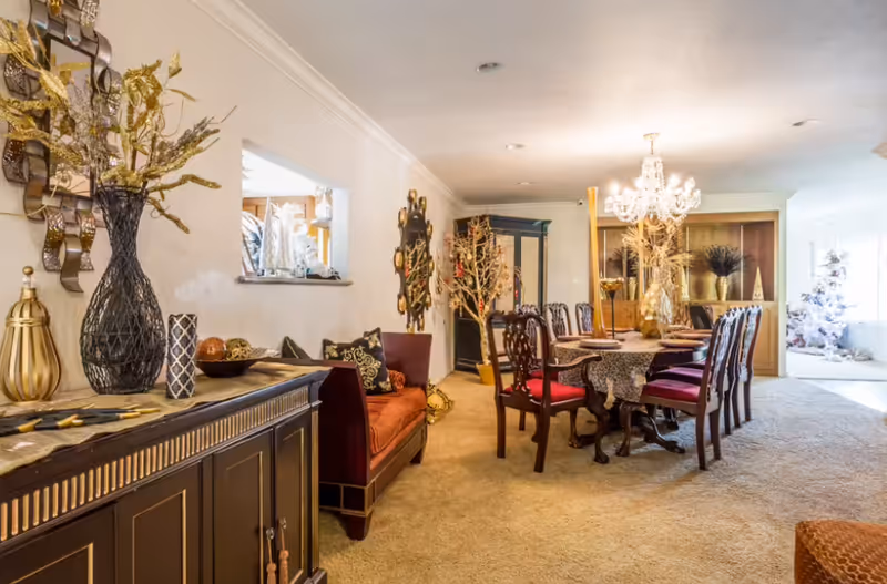 Ornately decorated dining room with a long table, chandelier, upholstered chairs, and sideboard with decorative accents.