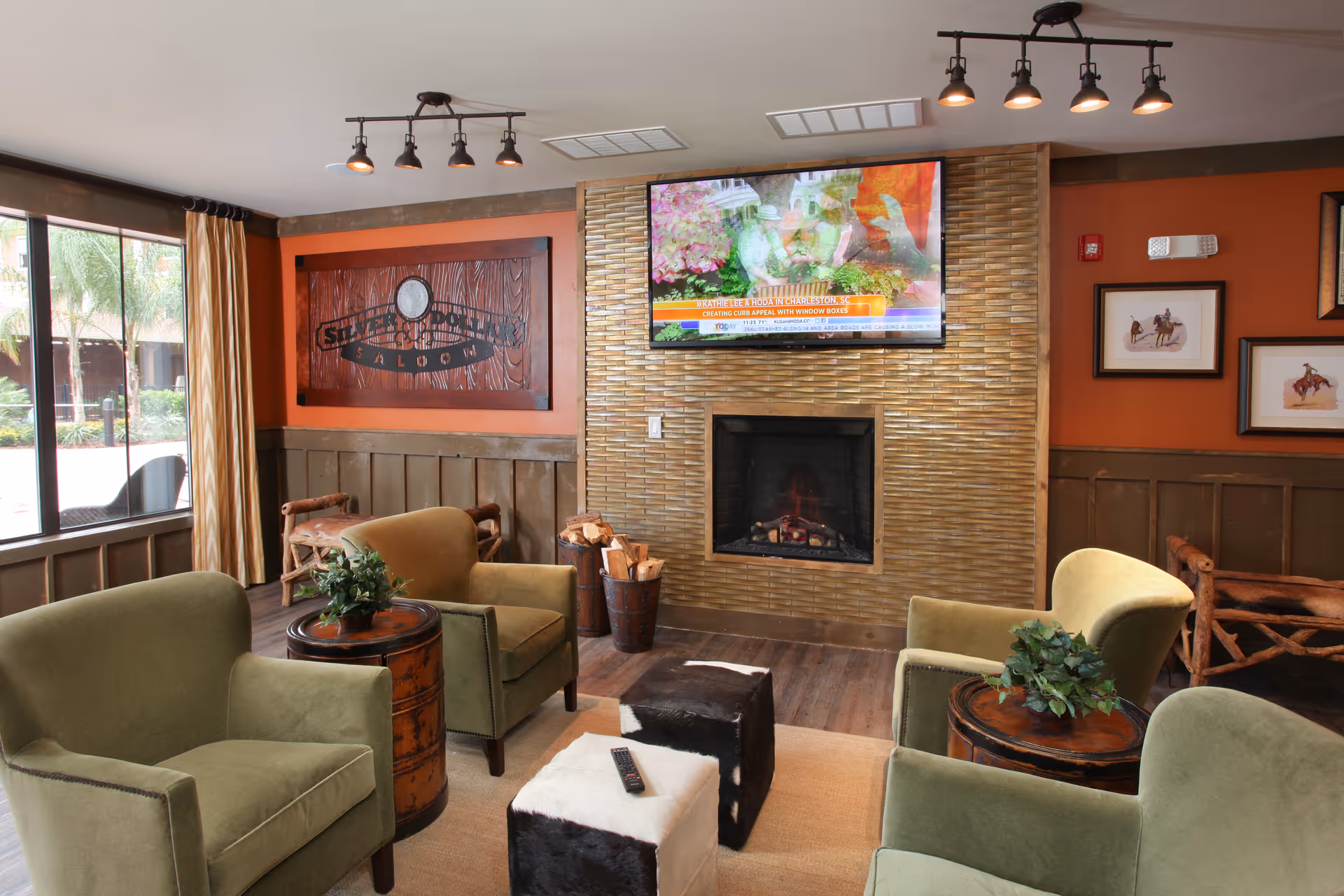 Cozy communal living room with green armchairs arranged around a fireplace and a wall-mounted TV.