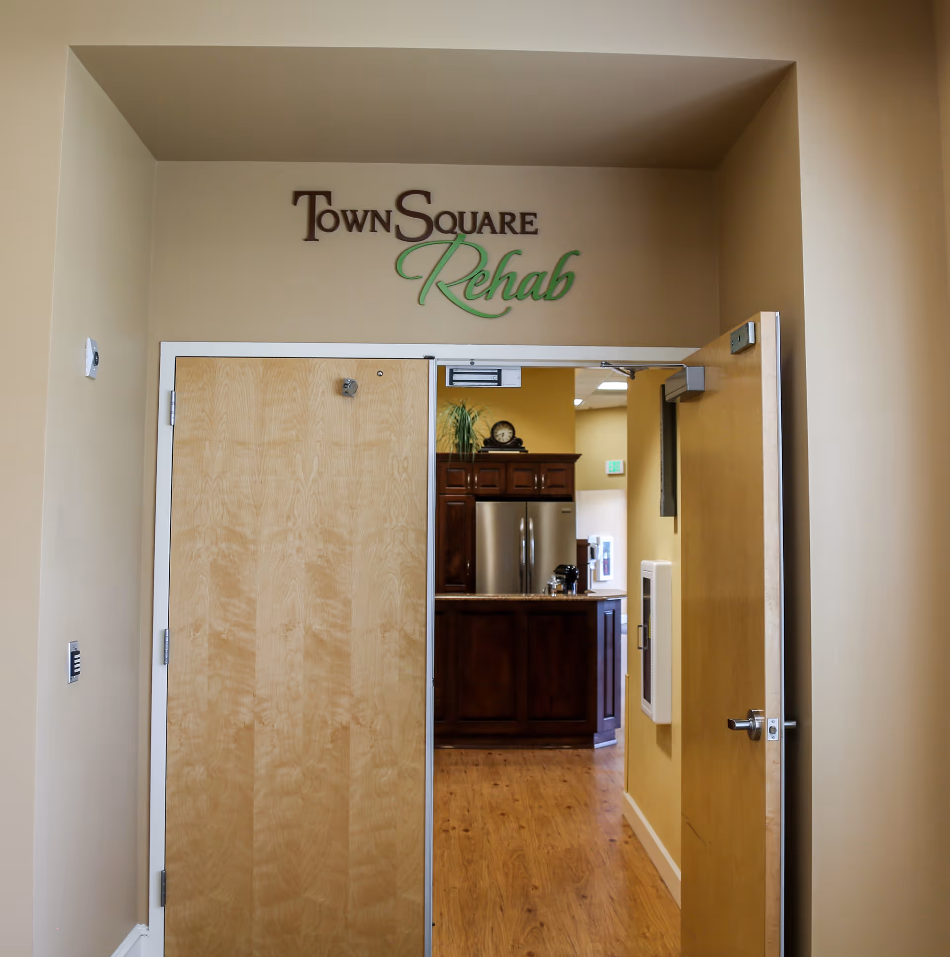 Open double doors with a 'TownSquare Rehab' sign above leading into a rehab area with wood floors and a kitchenette visible inside.