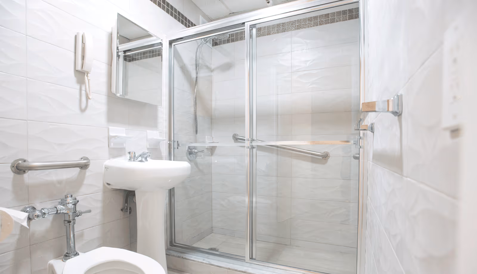 Bright accessible bathroom with a pedestal sink, toilet, grab bars, and a sliding-glass shower enclosure.