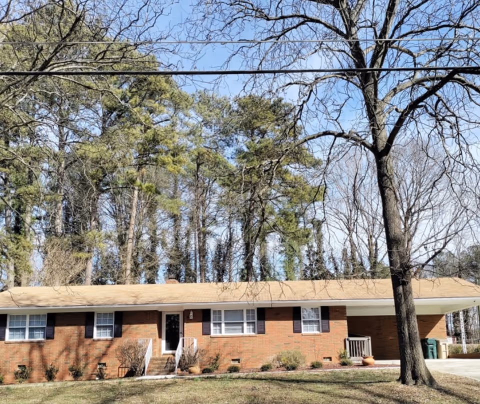 Single-story brick senior living building with front entrance, shrubs, and large trees.