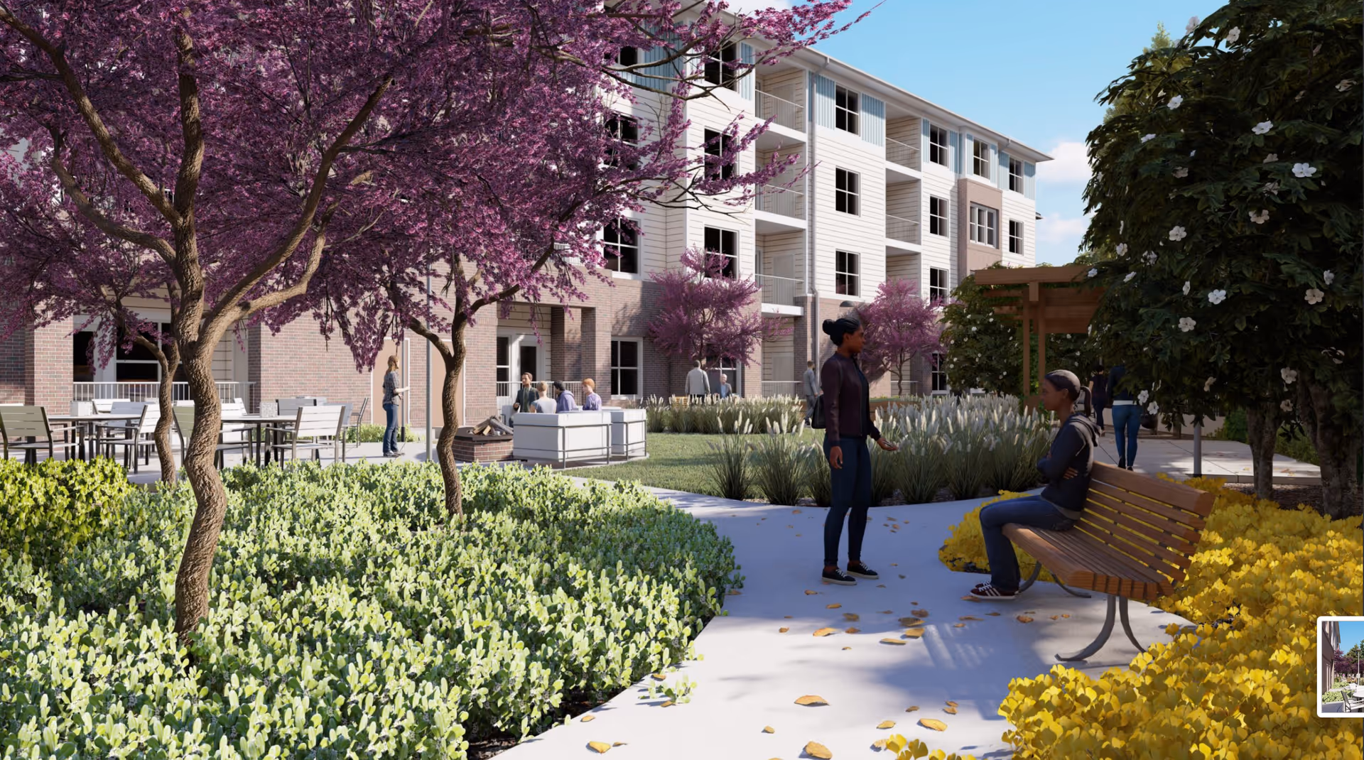 Outdoor garden area at Acclaim at Cary Pointe with people socializing. There are purple flowering trees, green shrubs, yellow flowers, a wooden bench with a person sitting, and a multi-story building in the background.