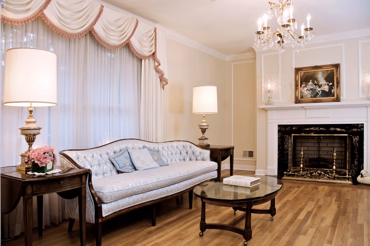 A well-decorated living room with a blue upholstered couch, table, lamps, and a fireplace.