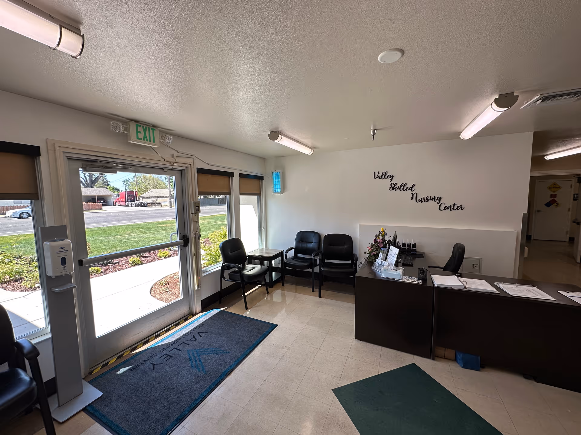Reception lobby of Valley Skilled Nursing Center with glass front doors, a seating area, and a reception desk under a wall sign.