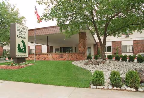 Front entrance of Berkley Manor Care Center with sign, flag, and landscaped pathway.