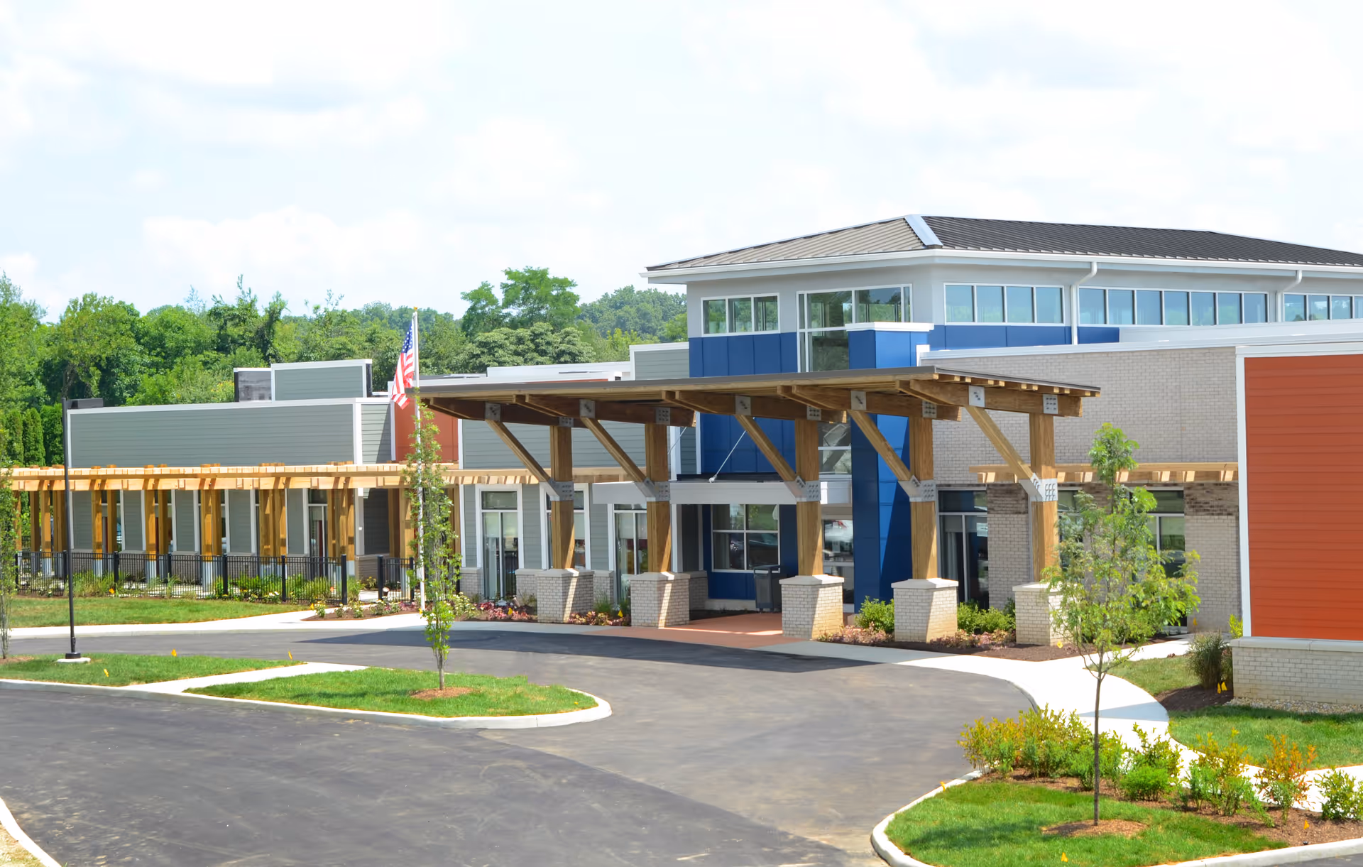 Entrance and covered porte-cochere of a modern senior living facility with landscaped driveway and an American flag.