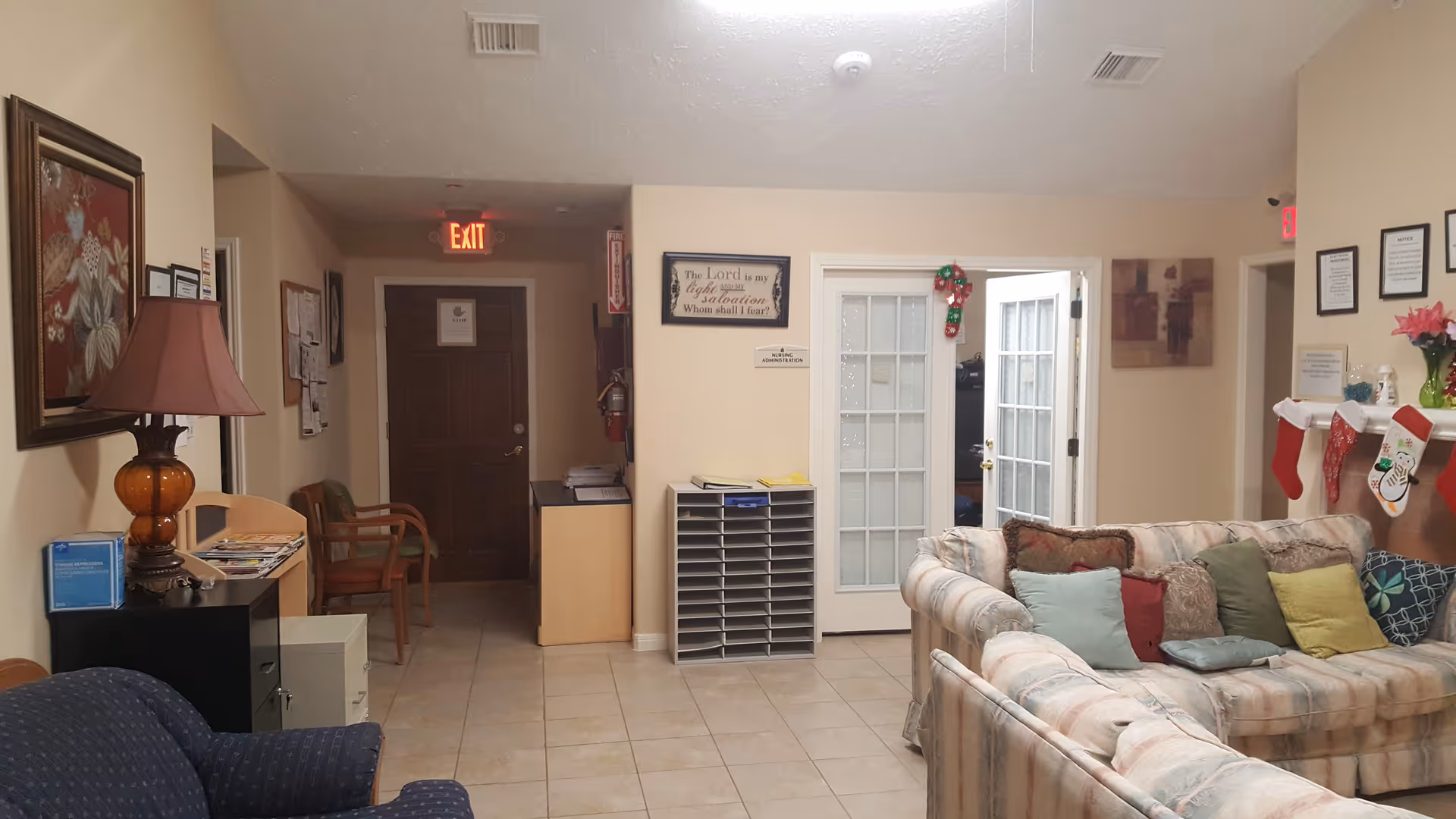 A cozy communal living room in an assisted living facility with sofas, chairs, a lamp, mail cubbies and holiday stockings.