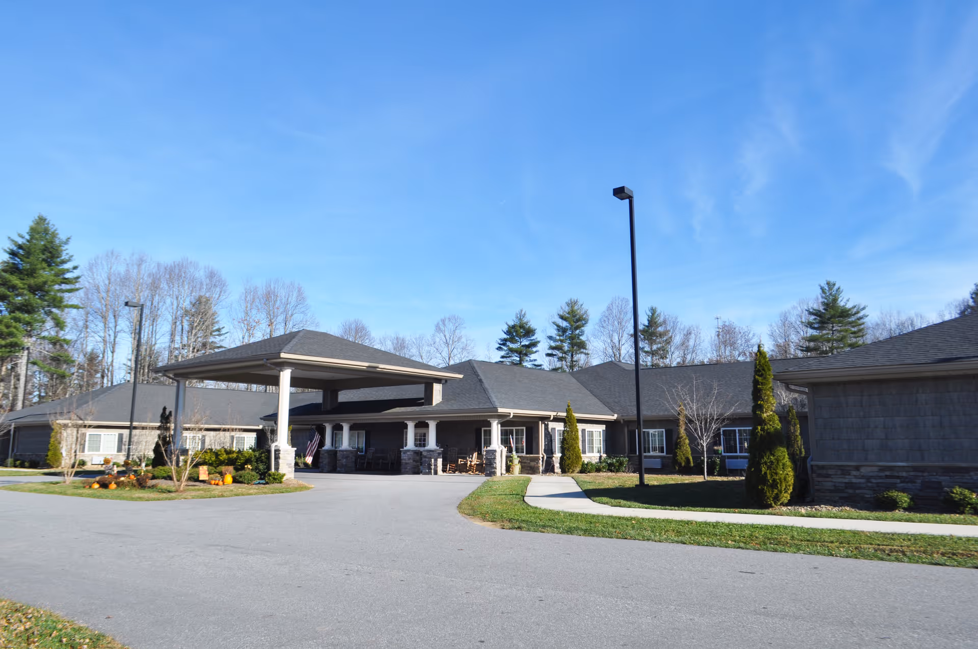 Exterior view of Mitchell House, a single-story building with a covered entrance driveway, surrounded by trees and landscaping under a clear blue sky.