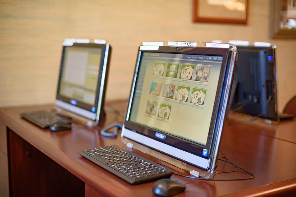 Two all-in-one desktop computers with keyboards and mice on a wooden table in a communal computer station.