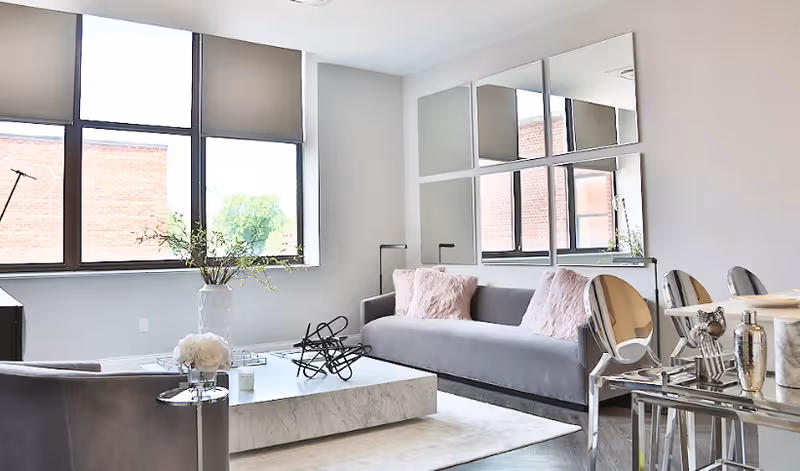 Bright modern living room with gray sofas, a marble coffee table, mirrored wall panels and large windows.